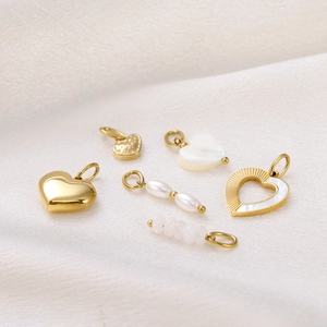 Detail view of heart pendants and pearl charms on silk, made of gold-plated steel and shell