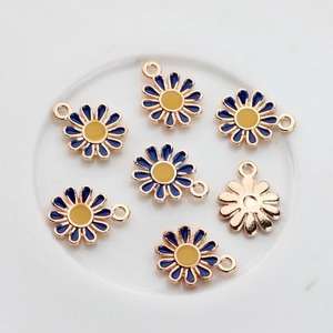 Blue and yellow enamel daisy flower charms with gold edges arranged on a white plate