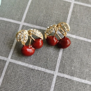 Détail de boucles d'oreilles cerises avec émail rouge, feuilles d'or et cristaux