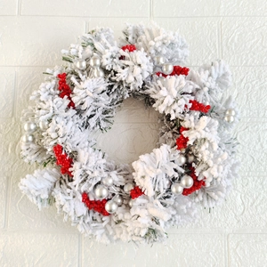 Cedar Christmas wreath with red berries and silver balls on a white brick background