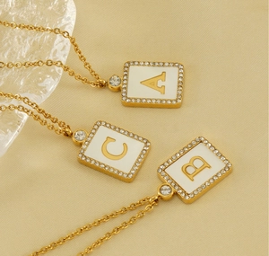 Detail of square gold necklaces with A, B, and C initials set in white shell and zircon