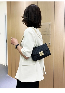 Close-up of black quilted chain bag with elegant gold clasp on a model's shoulder