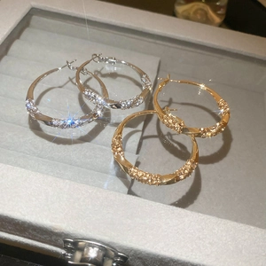 Detailed view of twisted gold and silver hoop earrings with pavé set crystals in a jewelry box