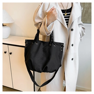 Close-up of a large black canvas tote bag with adjustable strap and metal rivet details