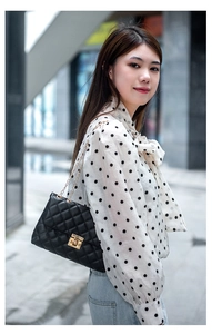 Close-up of black quilted shoulder bag with gold chain strap and metal swivel lock