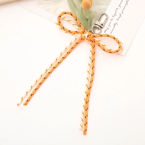 Detail of orange and white braided bow keychain with silver metal lobster clasp on a desk