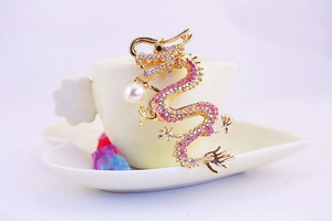 Detailed view of a golden dragon keychain with pink rhinestones and a white pearl accent