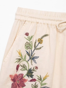 Detail of cream linen shorts featuring colorful floral embroidery and drawstring waist
