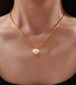 Close-up of elegant gold snake chain necklace with a large white pearl pendant on neck