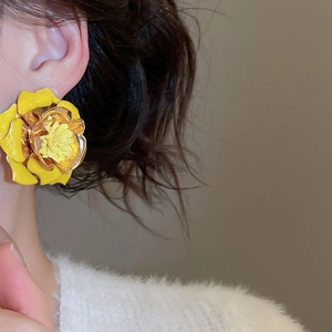 Gros plan d'une boucle d'oreille fleur 3D jaune avec un pistil en métal doré sur un modèle