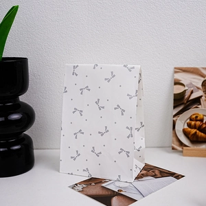 White paper gift bag with grey bow and polka dots pattern on a minimalist desk
