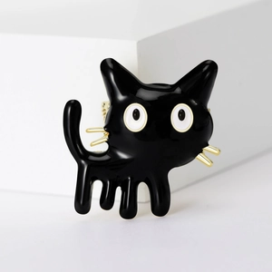 Close-up of black enamel cat brooch with gold whiskers on white geometric background
