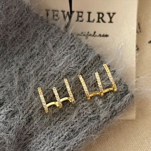 Golden three-row stud earrings with white zircon on grey knit fabric background