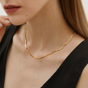 Close-up of elegant gold layered snake chain necklace worn by a model on black vest