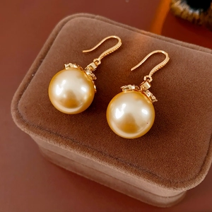 Détail de boucles d'oreilles perles dorées avec couronne sur un écrin en velours marron