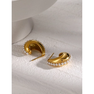 Macro shot of gold C-shaped hollow earrings with white pearls on textured stone