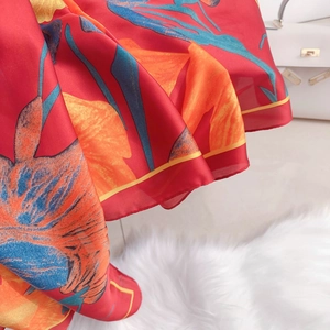 Detail view of red silk-like scarf featuring orange and blue floral patterns and light fabric
