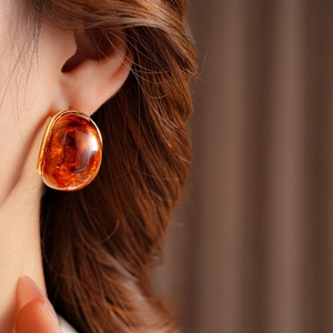 Macro shot of amber resin earrings with fine gold metal edges on a brown background