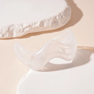Detailed view of irregular wavy white acrylic cuff bracelet on stone pedestal