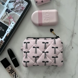 Pink quilted makeup bag with bow print and golden heart zipper pull on marble background