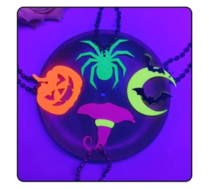 Close-up of four fluorescent Halloween felt pendants glowing under UV light in a dark party setting