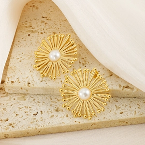 Golden sunburst flower stud earrings with central pearl on elegant stone background