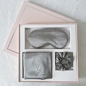 Detailed close-up of silver silk sleep set with eye mask and scrunchie in a pink gift box