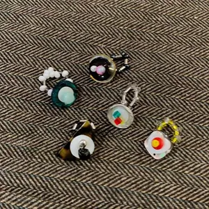 Detail view of five retro beaded elastic rings with poached egg charms on herringbone fabric