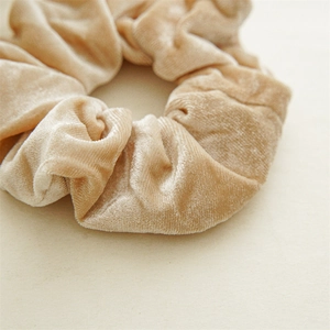 Dettaglio macro dello scrunchie in velluto champagne con trama morbida e lucentezza della seta