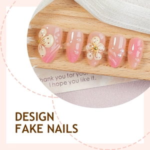 Pink gradient fake nails with 3D floral designs and pearls on a wooden display