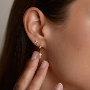 Close-up of golden cross earrings set with zircon stones on model's ear