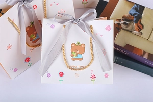 Detail of white cartoon bear gift bag with golden handles and grey satin ribbon bow
