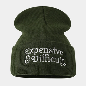 Close-up of white 'Expensive & Difficult' embroidery on dark green knit beanie