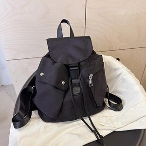 Detail of black nylon backpack featuring buckle closure and dual asymmetric front pockets