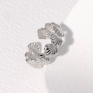 Close-up of shell-shaped silver stainless steel ring on a textured white surface