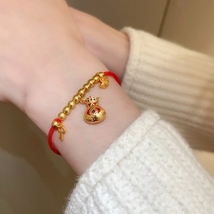 Gros plan d'un bracelet tressé rouge avec perles dorées et breloque sac de fortune