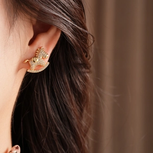 Close-up of golden horse-shaped stud earrings with sparkling rhinestones on a model