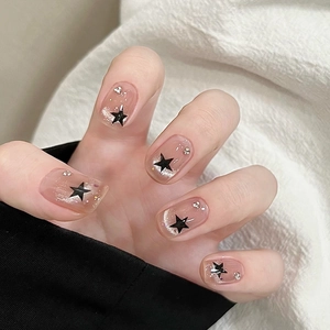 French cat-eye press-on nails in nude pink with black stars and glitter details