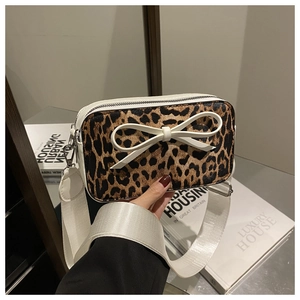 Detail showing leopard print crossbody bag with white bow accent and wide shoulder strap