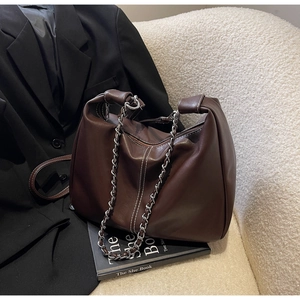 Detail of dark brown leather shoulder bag with silver chain and white stitching