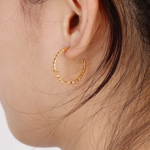 Detail of a C-shaped hollow golden earring with geometric Cuban chain texture
