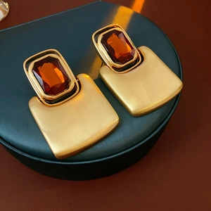 Macro view of gold rectangle matte earrings with amber faceted gemstones on a stand