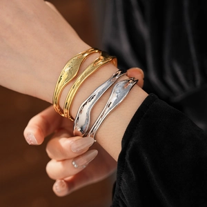 Close-up of gold and silver irregular pleated open bangles with lava texture on a model