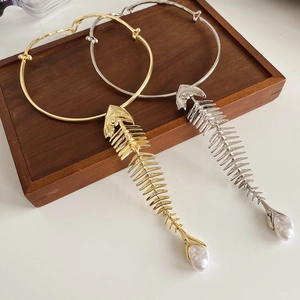 Close-up of gold and silver fishbone pendant necklaces with pearl accents on wood tray