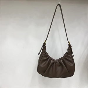 Detail of dark brown pleated crescent bag showing PU leather texture and shoulder strap