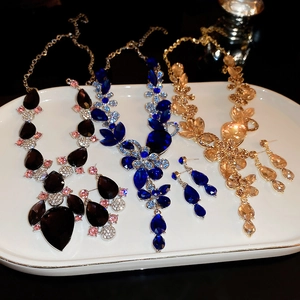 Three elegant crystal jewelry sets in blue, black, and gold displayed on a white plate
