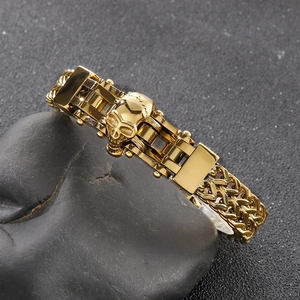 Close-up of golden skull biker chain bracelet displayed on natural black stone props