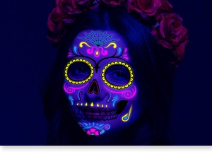 Close-up of Day of the Dead skull face tattoos glowing under UV light with neon colors