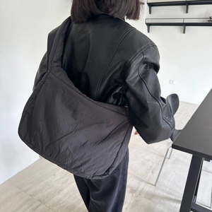 Detail of a soft puffy black nylon tote bag worn by a model in casual setting