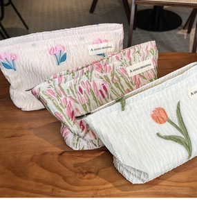Three canvas cosmetic bags with tulip patterns displayed on a rustic wooden table surface